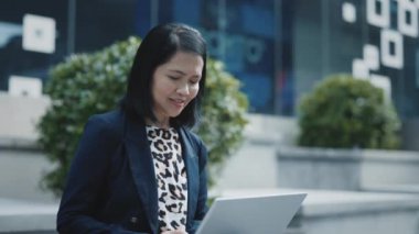 Neşeli Asyalı Eğitmen Mesafesi çalışıyor, Resmi Giysilerle Mesajlaşıyor, Açık havada Oturuyor. Dizüstü bilgisayar kullanan güzel, pozitif iş kadını. Halk ve Teknoloji Konsepti.