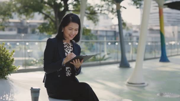 Занятая Привлекательная Азиатка Сидящая Одна Снаружи Отмечающая Свои Мысли Газете — стоковое видео