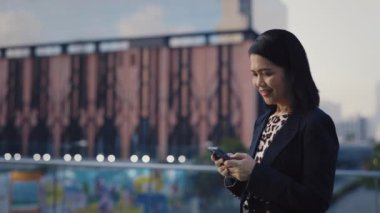 Caddenin Dışında Duran Kıdemli Kadın ve Akıllı Telefon 'da Mesaj. Gülümseyen Ofis İşçisi Kadın Chat 'te iş arkadaşlarıyla sohbet ediyor. Halk ve Teknoloji Konsepti