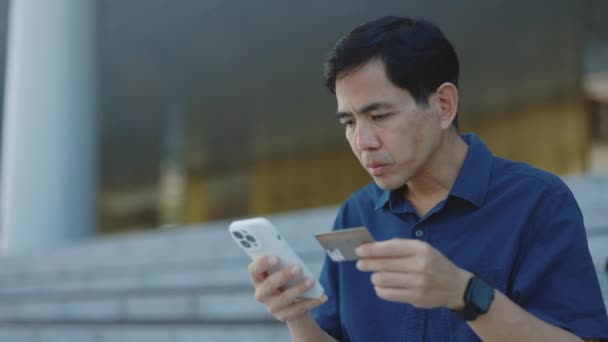 Serious Asian Businessman Sitting Using Smartphone Credit Card Buying Online — Vídeo de stock