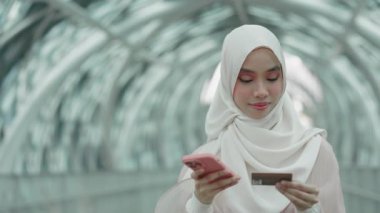Hijab 'daki Genç Olumlu Müslüman Kadın İnternetten Alışveriş Yapıyor, Dışarıda Dururken Akıllı Telefon' dan Kredi Kartı Numarasını Giriyor. Güzel İslamcı Kız Vergileri ödemek için kredi kartı ve akıllı telefon kullanıyor.