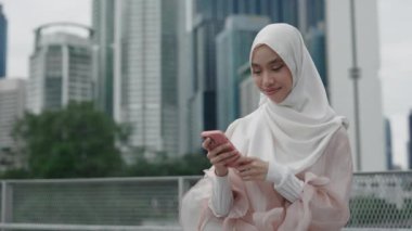Genç, güzel bir kadın, başörtüsü takıyor, dışarıda duruyor ve Smartphone kullanıyor, Online Kitap okuyor. Sokaktaki Müslüman Kadın İnternet 'te geziyor, Sosyal medyada Videolar seyrediyor.