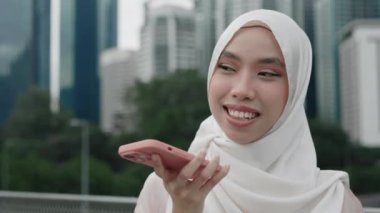Gülümseyen kadın caddede dururken tesettür kaydı takıyor. Güvenilir Müslüman Kadın Arkadaşlarıyla Sesli Sohbet Kullanarak İletişim kuruyor. Halk ve Teknoloji Konsepti