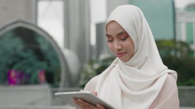 Başörtüsü 'ndeki şık Müslüman Kız Tablet Kullanıyor, Çevrimiçi İçeriği Dışarıdayken Gözden Geçiriyor. Moda İslamcı Kadın İletişim ve Eğlence İçin Tablet Kullanıyor. Halk ve Teknoloji Konsepti