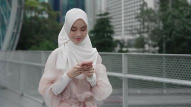 Gülümseyen Arap genç kız caddenin dışında duruyor ve cep telefonu kullanıyor. Güzel Bayan Başörtüsü Giyiyor ve Grup Sohbetindeki Arkadaşlarla Geleneksel Giysiler Mesajlaşıyor. Halk ve Teknoloji Konsepti