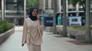 Zarif İslami Kadın yürüyüşe çıktı ve cep telefonuna sesli mesaj bıraktı. Etrafta dolaşırken tesettürlü kadın cihaza doğru konuşuyor. Teknoloji ve Günlük Yaşam Sahnesi. Halk ve Teknoloji Konsepti