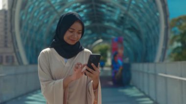 Modern Binanın Yakınındaki Güzel Müslüman Kadın Akıllı Telefonunu Kullanıyor. İnternette tesettürlü cep telefonu ve sörf yapan genç bir kız. Halk ve Teknoloji