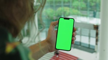 Uzun saçlı bir adam cep telefonunu elinde tutuyor ve pencereye yakın boş renkli ekranı var. Genç kişi evde akıllı telefon ve model sergisi kullanıyor. Reklam için tasarım şablonu