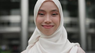 Geleneksel tesettürle gülümseyen, çeşitliliği ve modern yaşam tarzını yansıtan genç Müslüman bir kadının yakın plan portresi..