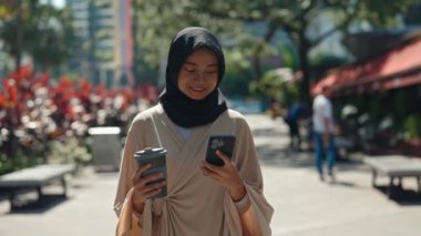 Genç, şirin, Müslüman, dışarıda yürüyen ve Smartphone ile mesajlaşan bir kadın. 