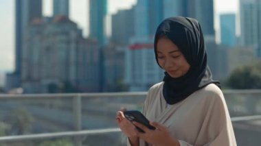 Siyah tesettürlü genç kadın dışarıda akıllı telefonuyla geziyor ve sörf yapıyor. Caddedeki Çekici Müslüman Kadın Evine Gidiyor ve İnternette Telefonla Kaydırıyor. Halk ve Teknoloji Konsepti