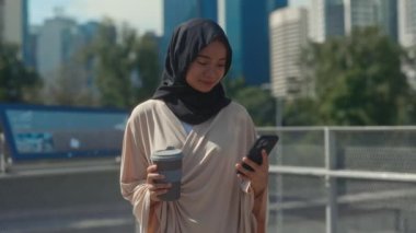 Güzel, Olumlu Müslüman Kız, dışarıda kahve molasında Smartphone 'u kullanıyor. Cep telefonundaki tesettürlü çekici kadın sosyal medyayı kaydırıyor. Halk ve Teknoloji