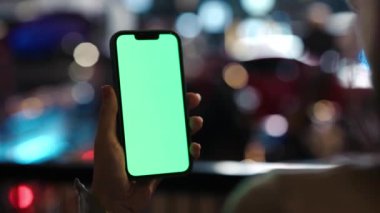 Kadın telefonu tutuyor ve Gece Sokağında duran Chroma Key 'e bakıyor. Ellerinde Yeşil Ekran Reklamcılık Alanı olan Akıllı Telefonu Tutan Genç Kız. Modelleme. Teknoloji İçeriği