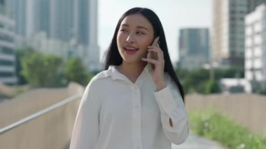 Asyalı iş kadını çalışıyor, Smartphone 'da konuşuyor, dışarıda yürürken yeni iş fikirlerini tartışıyor. Gülümseyen güzel ofis kızı cep telefonuyla konuşuyor iş görüşmesi iyi iletişimler