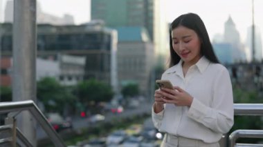 Mutlu Asyalı Kadın Dışarda Duruyor ve Arkadaşlarıyla Mesajlaşıyor ve İş Giysileri Giyiyor. Resmi Takım Elbiseli Arkadaş Canlısı Kadın Sokakta Sosyal Medya Sohbeti. Halk ve Teknoloji Konsepti