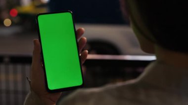 Kadın Gece Şehrinin Dışında Duruyor ve Telefonun Yeşil Ekranına Bakıyor. Kadın Elleri Cep Telefonu Kullanıyor, İnterneti Tarıyor, Krom Anahtar. Halk ve Teknoloji Konsepti