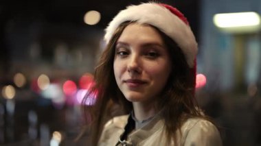 Beyaz kız portresi. Kış Şapkalı Mutlu Kız. Dışarıda dikiliyor ve tek başına gülümsüyor. Noel Baba Cap 'te yeni yılı kutlayan güzel pozitif bayan dışarıda kameraya bakıyor. Tatil Kavramı