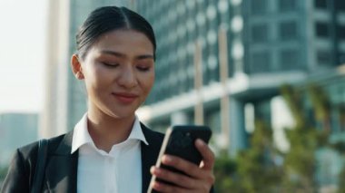 Güzel Pozitif Kız Dışarda Duruyor ve Telefonunda Video İzliyor, Ofis Giysileri Giyiyor. Gülümseyen İş kadını elinde akıllı bir telefonla Sosyal medya makalesi okuyor.