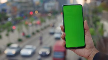 Chroma Key ile Telefonu Tutan Kadın El 'in Yakın Çekim Görüntüsü, Meşgul Bir Sokak Arkaplanına Karşı Bir Reklam Alanı. Telefonu Olan Kız ve Yeşil Ekran. Halk ve Teknoloji Konsepti