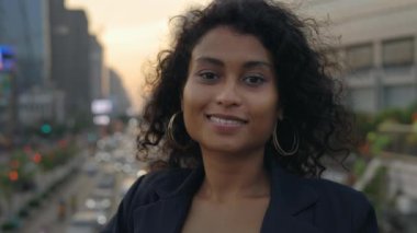 Şehrin arka planında duran kıvırcık saçlı güzel bir kızın portresi. Genç, çok ırklı iş kadını gülümsemeli kamera için poz veriyor. İnsanlar Konsepti