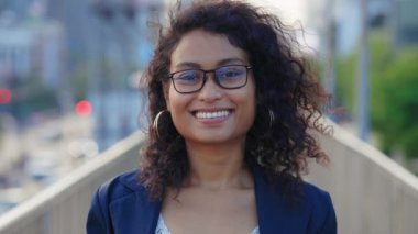 Güzel kıvırcık saçlı iş kadını, gözlüklü, dışarıda duruyor ve kameraya özgüvenle bakıyor. Açık havada Etnik Kız pozu. İnsanlar Konsepti