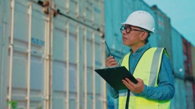 Endüstriyel Nakliyat İşçisi İnşaat Ekibinin Çalışmalarını İzlerken Dışarıda durup, Emirler verirken, Belgelerle Her Şeyi Kontrol Ederken. Dışarıda Walkie-Talkie ile çalışan meşgul kıdemli işçi