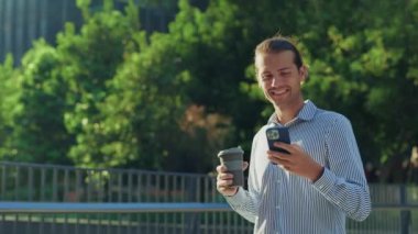 Yakışıklı iş adamı işten sonra parkta yürüyor, kahve kupası tutuyor ve iş konuşmalarında sohbet ediyor. Genç şirket sahibi kahve molasında akıllı telefonunu kullanıyor. Halk ve Teknoloji Konsepti