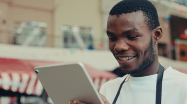 Sakallı Afro-Amerikan bir adamın portresi. Yemek reyonunda kafasını çevirirken akıllı tablet kullanıyor. Geniş gülümsemeli erkek garson, kafede duran el bilgisayarı siparişlerini kontrol ediyor.