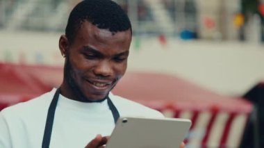 Akıllı tablet üzerinde çalışan, geniş gülüşlü Afro-Amerikan bir adamın portresi. Neşeli erkek yönetici kafedeki el bilgisayarındaki dijital menüyü okuyor. Adam servis çalışanı online siparişleri gözden geçiriyor