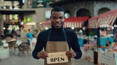 Afro-Amerikalı garsonun portresi açık tabela tutuyor müşterileri kafeye davet ediyor. Üniformalı, dişlek gülümsemeli erkek servis temsilcisi müşterileri yemek bölümüne buyur ediyor.