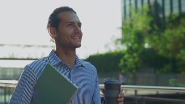 Neşeli bir iş adamı, elinde bir bilgisayar ve kahve fincanı ile dışarıda yürüyor. Neşeli, Kahveli Çekici Şirket Yöneticisi, Laptop Ofisi 'ni dışarıda tutuyor. İnsan ve İş Konsepti