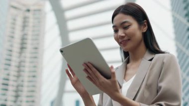 Mutlu Taylandlı kadın yöneticinin portresi. Sokakta tabletle internette geziniyor. Asyalı iş kadını taşınabilir bilgisayarla ticari verileri kontrol ediyor. Hanımefendinin molası var.