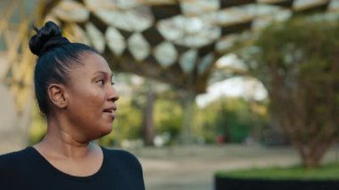 Dışarı koşan ve siyah giysiler içinde etrafa bakınan mutlu kadın. Etnik Yetişkin Koşucu Spor Yapıyor, Kilo Veriyor, Açık havada Kalori Yakıyor. Halk ve Spor Konsepti