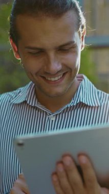 Dikey video. Genç Adam Tablet 'te Videolar Arasında Kayıttayken Dışarıda Gülümserken. Yakışıklı, pozitif avukat interneti kolaçan ediyor. Halk ve Teknoloji Konsepti