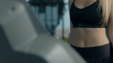 Atletik genç kadın modern spor kulübünde koşu bandında yürüyor. Zayıf vücutlu, kendine güvenen sporcu kadın spor salonunda yoğun antrenmana hazırlanıyor.