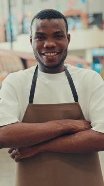 Kafede kolları çapraz duran Afrikalı Amerikalı garson portresi. Üniformalı genç erkek servis temsilcisi yemek bölümüne hoş geldin tebessümlü müşterileri davet ediyor.
