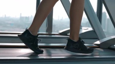 Spor ayakkabılı bir kadın spor kulübündeki koşu bandında pencereye yakın bir yerde koşuyor. Modern insanların aktif yaşam tarzı, genel fiziksel sağlığı kolay egzersizlerle geliştiriyor.