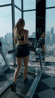 Sporcu kadın spor salonunda koşu bandında aynada yansımanın tadını çıkarıyor. Spor giyim sektöründe genç bir bayan spor kulübünün dikey videosunda aktif olarak kalori yakıyor.