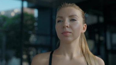 Modern spor salonundaki koşu bandında yürürken taze su içen genç bir kadının portresi. Atletik sarışın kadın spor kulübüne bakmayarak vücut şeklini düzeltiyor.