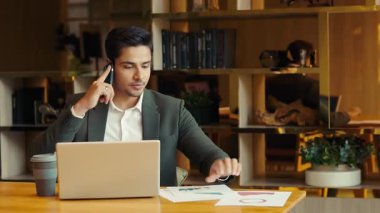 Hintli müdürün portresi diyagramlarla cep telefonuyla içeride konuşuyor. Meşgul erkek girişimci şirket ofisindeki masada oturan projeyi tartışıyor. İş iletişimi