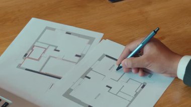 Mimar tasarımcı el, ahşap masa kapanışında muhafaza planlarına işaretler yazar. Tahta masadaki binaların çizimlerini top kalemle kontrol eden mühendis. İnşaat bürosu işi.