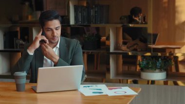 Mutlu Hintli iş adamının portresi cep telefonuyla konuşuyor bilgisayardaki verileri kontrol ediyor. Girişimci, müşterilerine danışmanlık yapar kahve ve çizelgelerle birlikte masada otururlar.