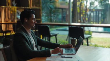 Kendine güvenen Hintli işadamı kişisel ofisteki bilgisayar aracılığıyla video çağrısına cevap veriyor. Genç girişimci online toplantıda ortaklarla konuşuyor. Çalışma masasının gölgesinde oturuyor.