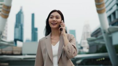 Modern şehirdeki neşeli Asyalı kadın şirket çalışanlarının portresi. Taylandlı kadın iş ortağıyla telefonda konuşmaktan mutlu. İş kadını sohbeti yürütür