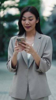 Genç Taylandlı kadının portresi sokaklarda akıllı telefon tutarken zafer işaretleri gösteriyor. Esmer Asyalı iş kadını kariyerinde ilerlemek için yeni bir fırsat olduğunu doğrulayan mesajı okuyor. Dikey video