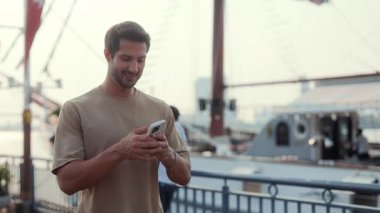 Lüks bir yatın önünde duran akıllı telefondaki gülümseyen Latin Amerikalı erkek mesajlarının portresi. İspanyol adam cep telefonuyla şehir limanında yürürken mesaj yazıyor. İletişim için aygıt