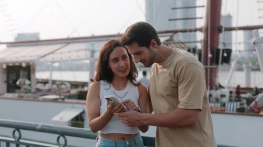 Genç Latin Amerikalı çiftin portresi, demirli modern yata karşı akıllı telefondan internette sörf yapıyor. Mutlu İspanyol erkek ve kadın şehir limanında romantik bir randevu için deniz yolculuğu kitabı.