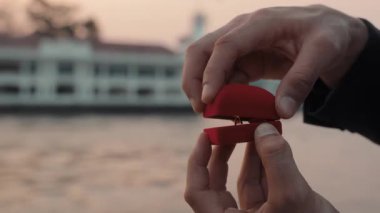 Erkek el, deniz limanına yakın çekimde yatta nişanlısına nişan yüzüğü vermek için kutuyu açar. Partner, romantik duygular için lüks mücevherler sunmayı teklif ediyor.