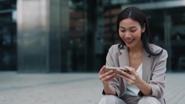 Şehir caddesinde canlı yayını izlerken zafer işaretleri gösteren Taylandlı kadın portresi. Neşeli Asyalı kadın akıllı telefondan yayınlanan spor takımının başarısını kutluyor