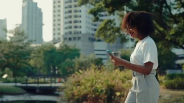 Afro-Amerikan kadın akıllı telefon ve kahve fincanı taşıyor. Şehir parkında yürüyor. Genç bir kadın cep telefonuyla sohbet ederken ofis binalarının yan görüntüsünü okuyor.